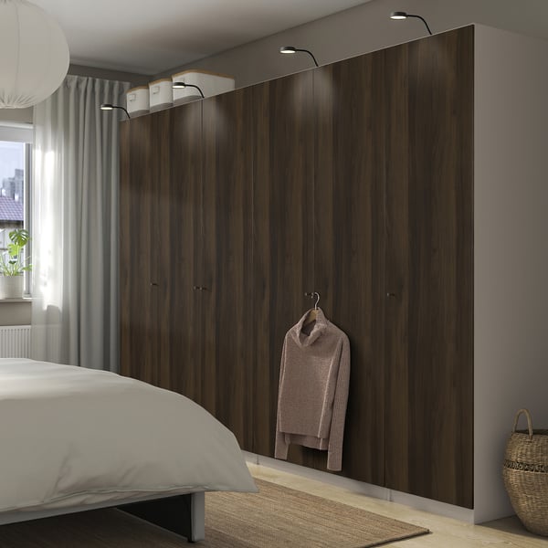 Modern bedroom with dark brown PAX wardrobe, soft-close doors. Sweater on hook, white bed, window with curtains, wicker basket.