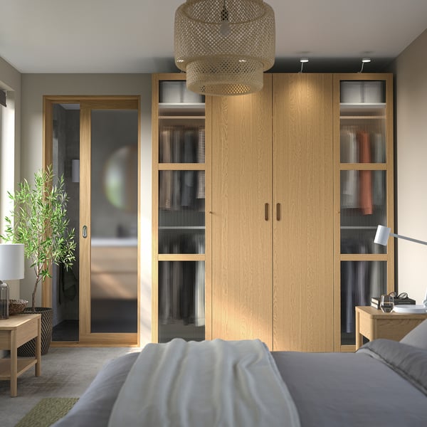 Bedroom with PAX wardrobe, white bed, desk, plant, wicker lamp.