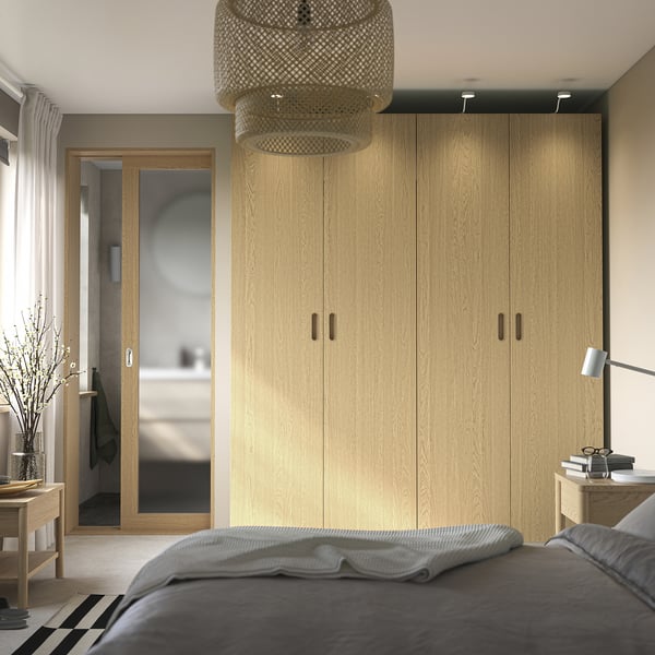 Modern bedroom tall light-wood PAX closet, sleek design, grey bedding, hanging light fixture, and side table with decor.
