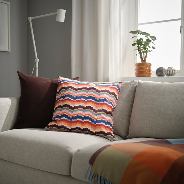 Cosy corner with grey sofa, colourful cushions, lamp, plant, and spheres.