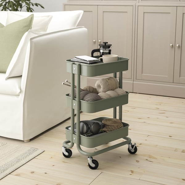 A green ikea RÅSKOG trolley with three shelves. Its small, fits under desks, and holds various items.