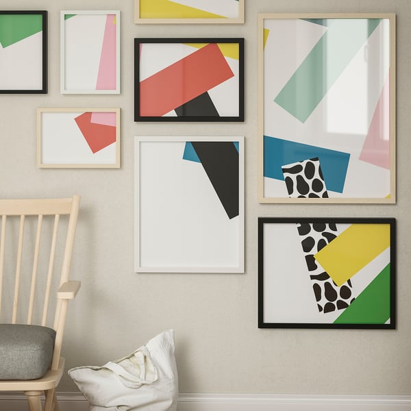 Gallery wall with colourful geometric art in wood & black RÖDALM frames, sizes varied, light wood chair with grey cushion.