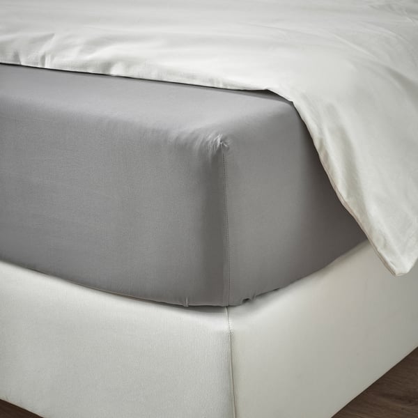 Neatly made bed sheets with a smooth, grey top sheet and white pillowcases on a mattress. The elastic-edged fitted sheet holds it securely in place.
