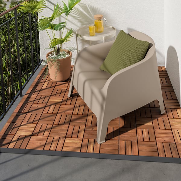 Cosy balcony with beige RUNNEN chair, green pillow, small round table, two yellow drinks, and large potted plant on wooden deck.