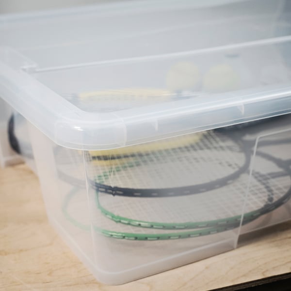 Clear plastic storage box with lid, containing two tennis rackets, showcasing durability and transparency.
