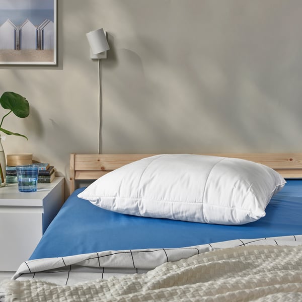 SENAPSMOTT pillow on blue bed, minimalist room with plant.