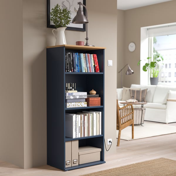 SKRUVBY black bookcase with wooden top, holding books & decor. Tall, fits corner of cosy living room, near beige walls & white furniture.