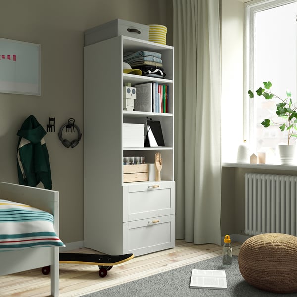 Grey and white SMÅSTAD bookcase with books, clothes, decor, a small bed, and framed art.