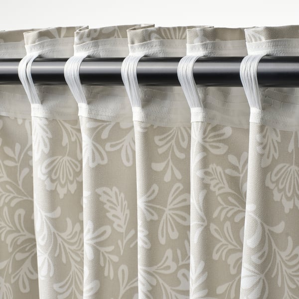 A close-up of beige floral curtains with white patterns. They have loop tabs for rods, filtering light and offering privacy.