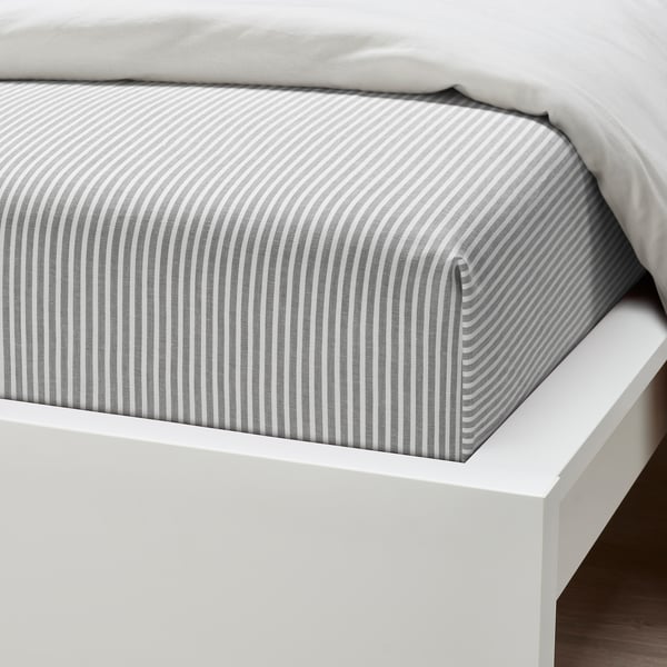 A neatly made bed with a light grey and white striped fitted sheet on a white bed frame.
