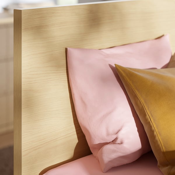 Close-up of a modern, well-crafted wooden headboard with smooth, light stains and pastel pillows against it, showcasing high-quality design.