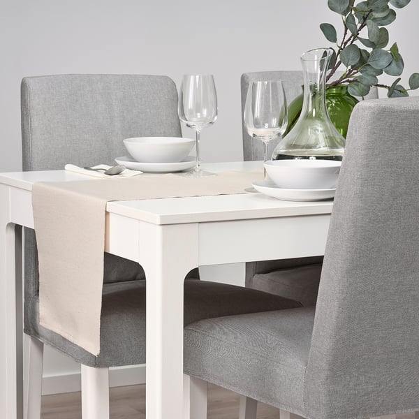 White dining table with grey chairs; set with bowls, plates, wine glasses, and green vase with plant.