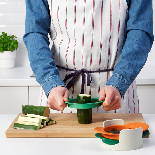 Person prepares courgette using a colourful kitchen gadget, which slices fruits and vegetables efficiently.