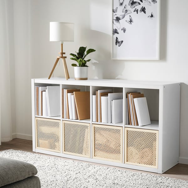 A white våltning cube organiser with books and decor. It includes a lamp, plant, and a butterfly poster.