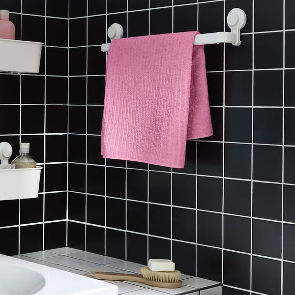 Bright pink VÅGSJÖN towel hangs on wall mount, smaller than adjacent bottle.