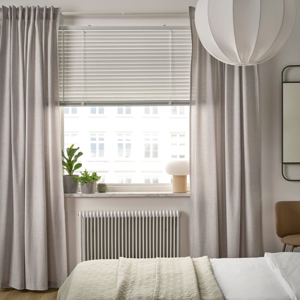 Modern bedroom with large VECKLARFLY blinds, light grey, covering wide window, matching curtains, potted plants, and a cosy bed.