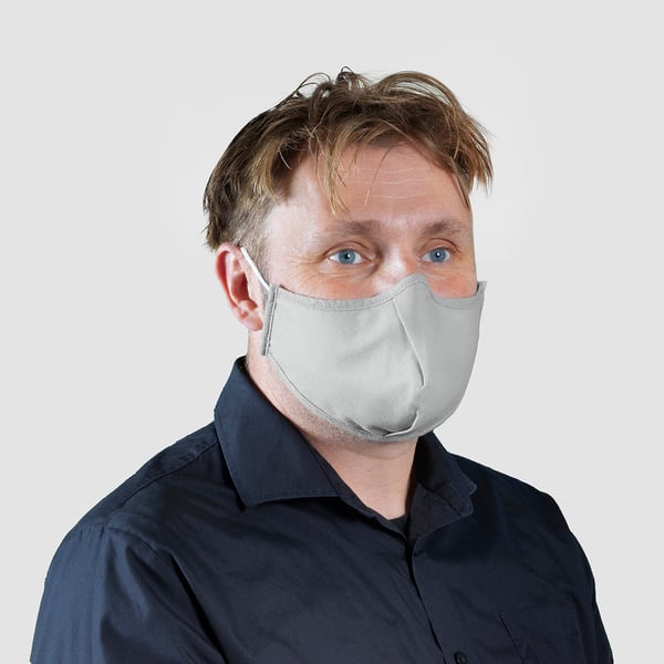 Person wearing light grey cloth mask over dark shirt, showcasing design and fit for personal protection.