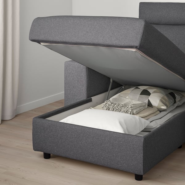 Gray upholstered sofa with storage compartment open, showing pillows inside.