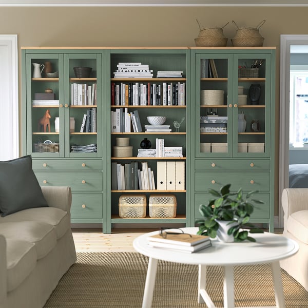 Серо-зеленый книжный шкаф HEMNES с книгами и декором между бежевыми диванами и белым столом