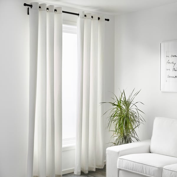 Минималистичная комната со светоблокирующими шторами MERETE на черном стержне, растением и стулом.