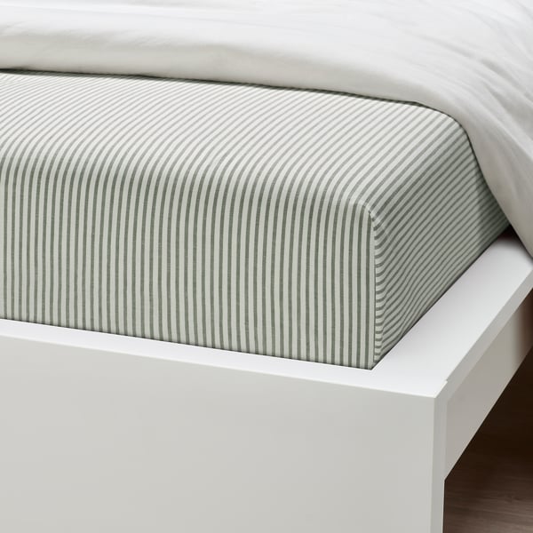 Полосатая хлопчатобумажная простыня на белом каркасе кровати, демонстрирующая гладкую текстуру и качественную ткань.