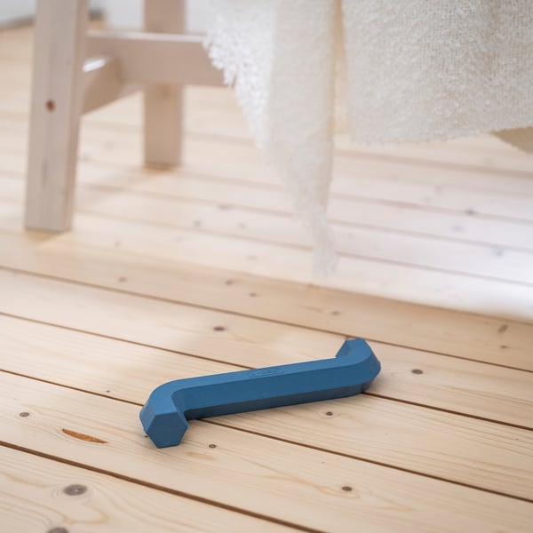 Игрушка для голубой собаки на деревянном полу, по форме напоминающая шестигранный ключ. Входит в линейку UTSÅDD от IKEA.