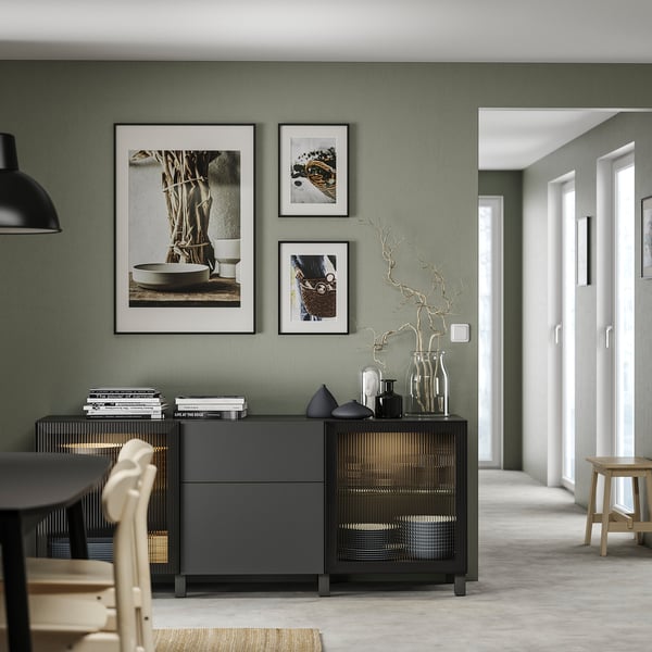 Modern living area with grey BESTÅ storage unit, featuring adjustable shelves, black vases, and framed art on sage green wall.
