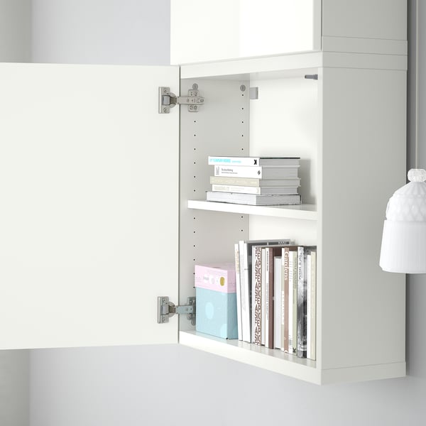 Open white cabinet with two shelves, containing colorful books and a blue box. The cabinet is wall-mounted, part of the BESTÅ storage system by ikea.