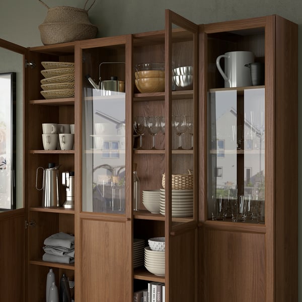 Wooden display cabinet with glass doors showcasing dinnerware, glassware, and pitchers. Adjustable shelves and dust-free storage.