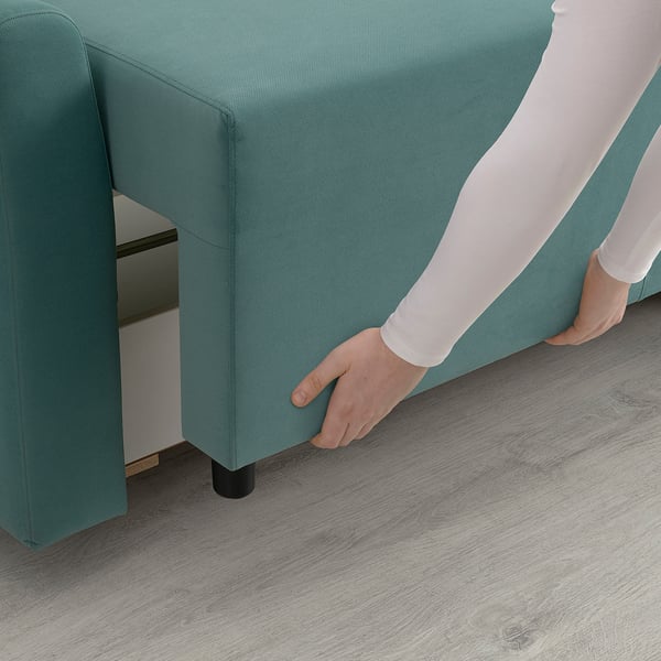 Person adjusting under-section of a green sofa. The sofa has a hidden storage compartment.