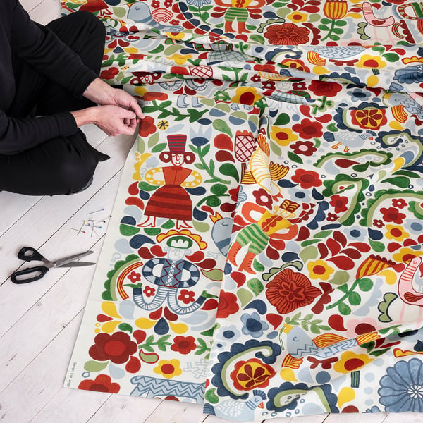 Person crafting with colourful, patterned fabric on wooden floor. Scissors and pins nearby.