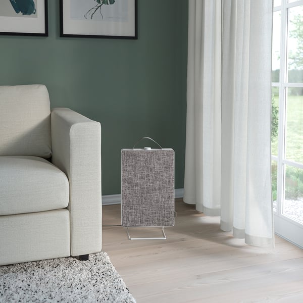 Small, modern grey air purifier beside white couch.