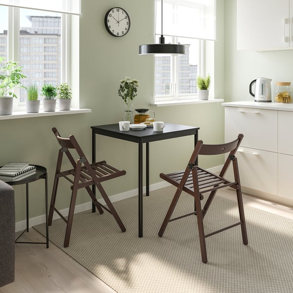 Small black FRÖSVI table & chairs, perfect for cosy kitchens. Light, foldable design with wooden seats. Bright room with plants & coffee setup.