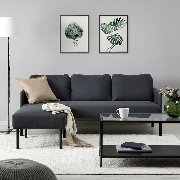 Modern living room with GLOSTAD grey sofa, thick cushions, plant art, glass coffee table, and floor lamp. Minimalist and contemporary.