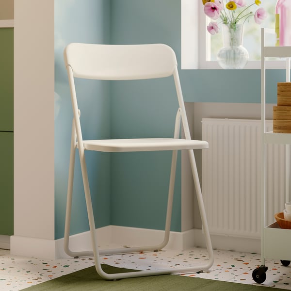 White GUNDE folding chair in cosy room with green cabinets. Ideal for small spaces.