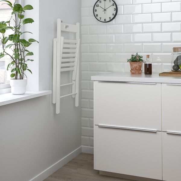 Modern kitchen with white cabinets, plants, and a clock. A HAUGA drop-leaf table folded against the wall, ideal for space-saving.