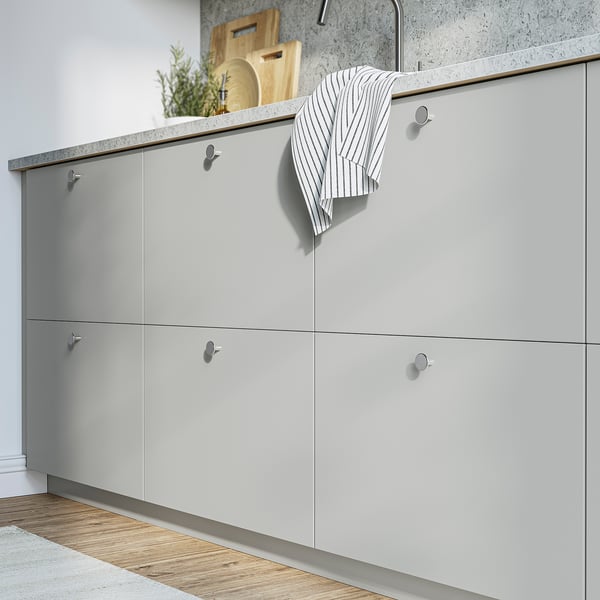 Modern grey kitchen cabinets with round handles. Striped towel, cutting boards, and plant on counter.