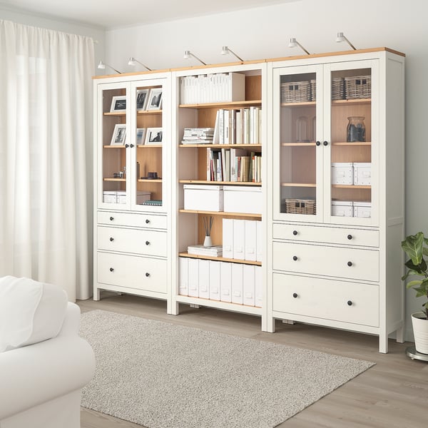 White HEMNES unit with glass doors & drawers, holding books & decor, minimalist & room-dominating.