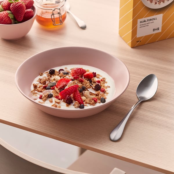 A bowl of granola with yoghurt, strawberries, and other berries is shown on a table with a spoon.