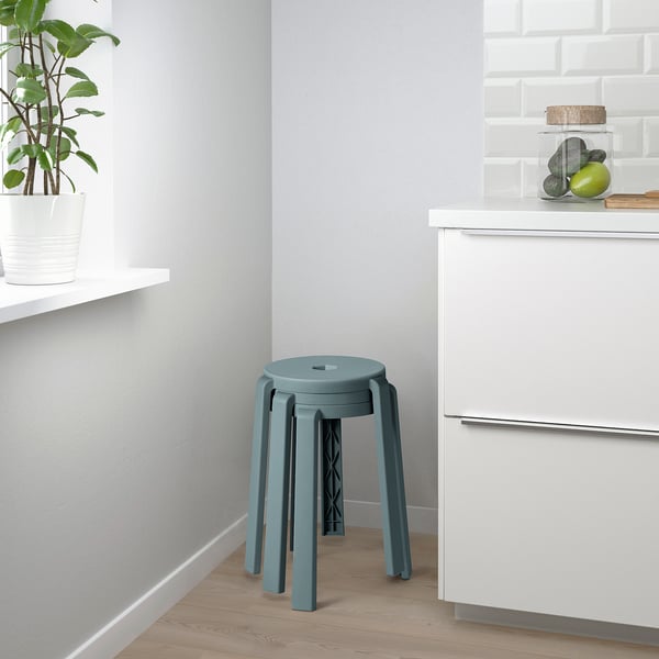 Modern kitchen with blue stool, white cabinets, green plant, and fruit jar.