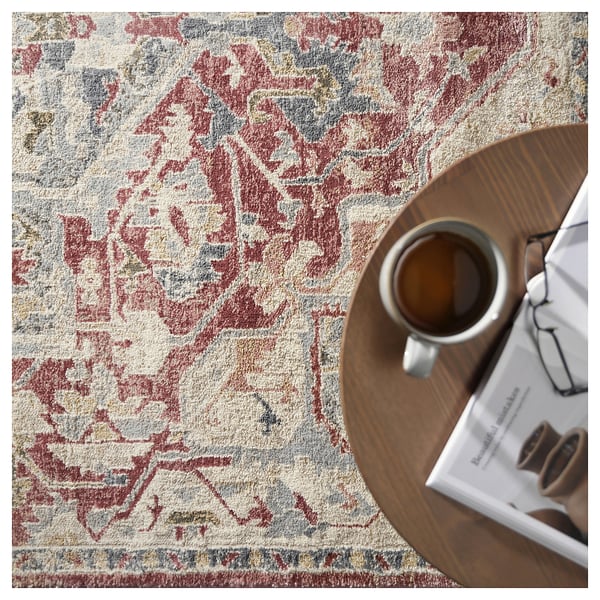 Decorative rug named JÄRNVÄG with pastel tones, floral design, placed under a wooden table with a mug and magazine.