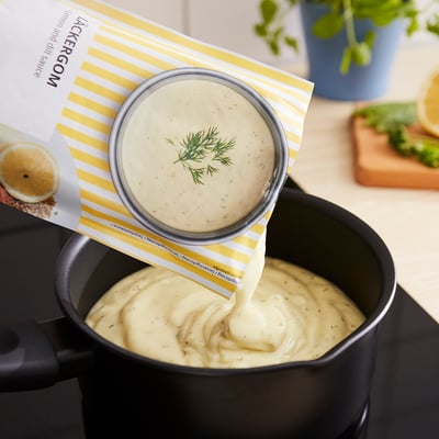 Image container pouring creamy sauce into pan. Yellow label reads LÄCKERGOM lemon and dill sauce.