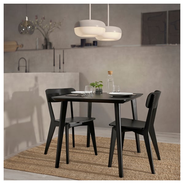 Modern black dining set with rectangular table and chairs. Sleek legs and simple design. Hangs pendant light above.