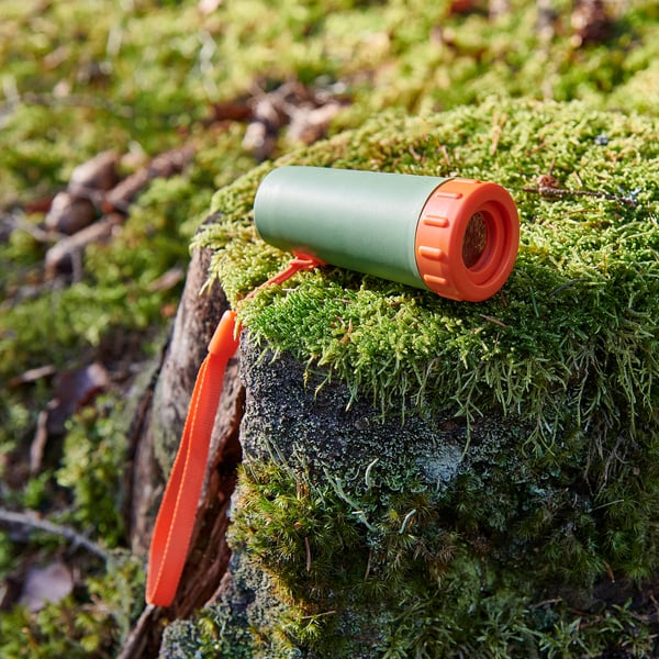 Green and orange mini monocular rests on moss-covered tree branch. Durable, compact design ideal for outdoor use.