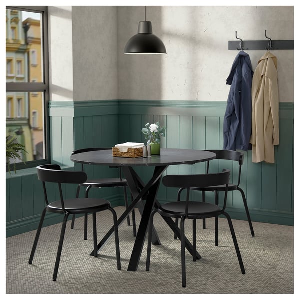 Modern dining setup with MARIEDAMM black round table and chairs, hanging coats, pendant lamp, and green-painted wooden wall.