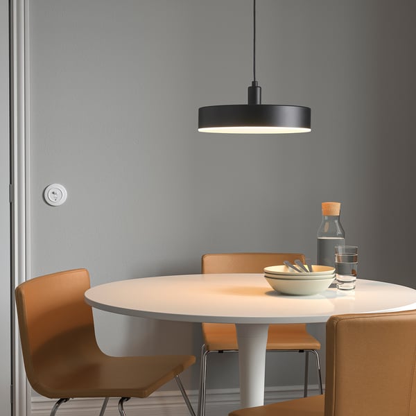 Modern dining setup with NYMÅNE pendant lamp over round table and orange chairs, holding a bowl, glasses, and a bottle.