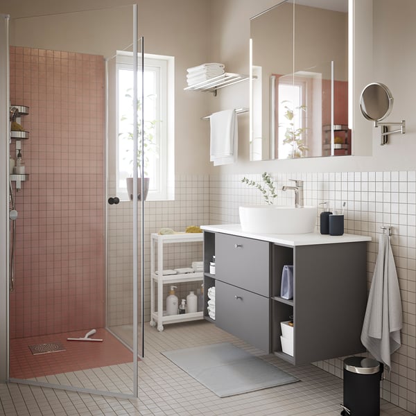 Modern bathroom with white walls, pink tiles, grey storage, large mirror, vessel sink, OPPEJEN glass shower door.