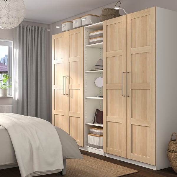 Modern bedroom with large light wood PAX wardrobe, minimalist decor, stylish chandelier, grey curtains, and cosy bed.