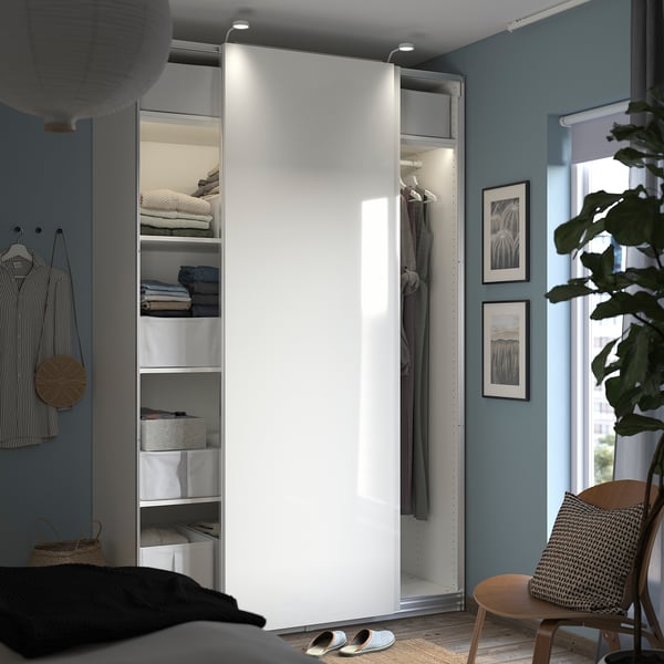 Modern blue bedroom with white PAX wardrobe and sliding doors. Art, plants, and a wicker chair.
