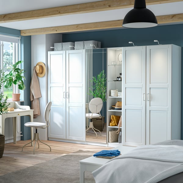 Large white PAX wardrobe with mirrored doors, reflecting chair and shelves, in minimalist room with light furniture.